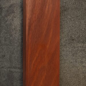 A polished rectangular block of Jarrah wood with rounded edges, showing a rich reddish-brown color and fine grain pattern, placed on a gray textured surface.